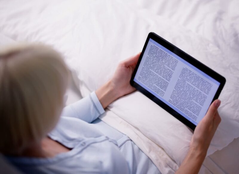 starija osoba leži u krevetu i čita e knjigu