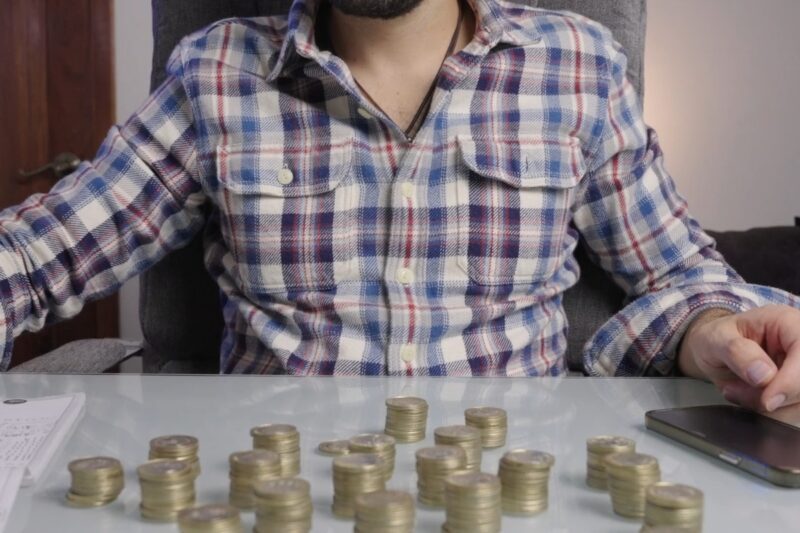 prikaz momka koji sedi za stolom na kom su kovanice sa novčićima