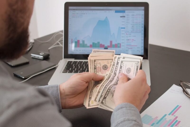 prikaz osobe koja koristi laptop i broji novac u ruci