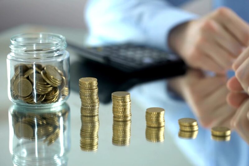 prikaz osobe koja slaže novčiće jedne do drugih po večilici i teglice pune novčića pored