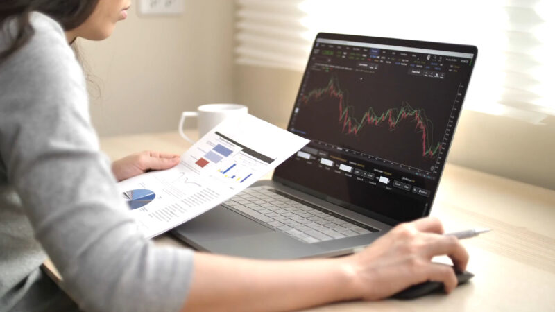 prikaz devojke koja koristi laptop i drži papir u ruci