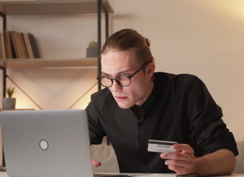 muška osoba gleda u monitor začuđeno i drži kreditnu karticu u ruci