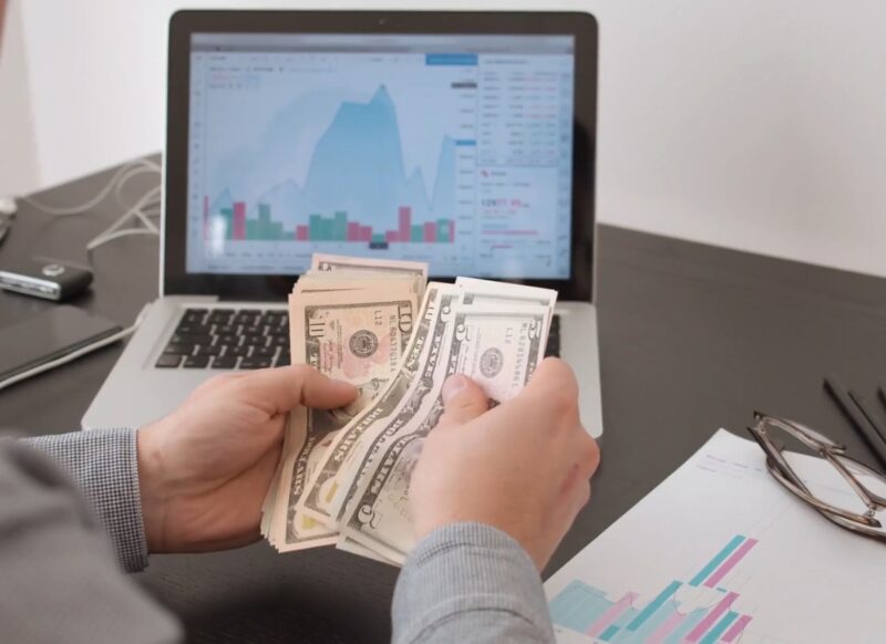 prikaz osobe koja broji novac i ispred njega stoji laptop